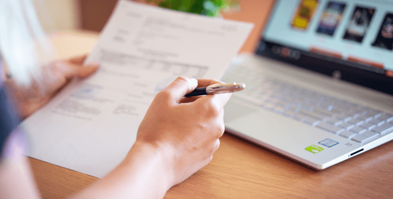 Planejamento financeiro, documento e computador portátil com tela exibindo ofertas digitais de serviços financeiros em ambiente de trabalho.