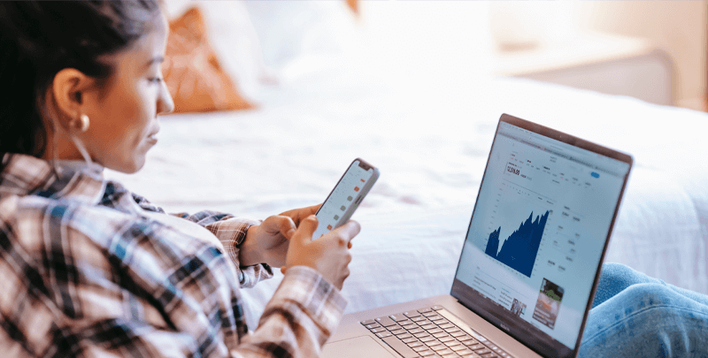 Relatório financeiro em digital, mulher analisando dados no celular e laptop com gráficos de crescimento.