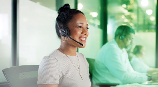 Atendente de suporte ao cliente em call center usando headset em ambiente de atendimento.