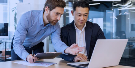 Profissionais de negócios analisando documentos e usando laptop em escritório moderno, focados em soluções fiscais e tributárias com Dootax.