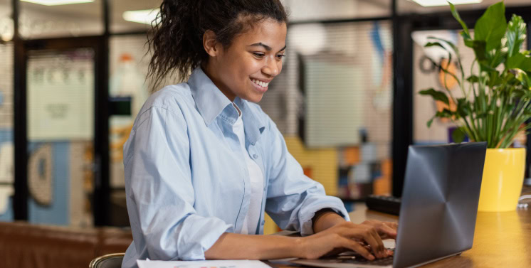 1. Mulher feliz usando laptop em escritório, foco em soluções de gestão e tributos com Dootax, plataforma digital para facilitar sua rotina fiscal e tributária.