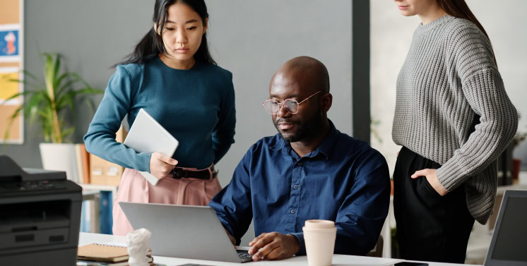 1. Homens e mulheres em reunião de trabalho utilizando laptop, com foco em soluções de gestão e consultoria empresarial.