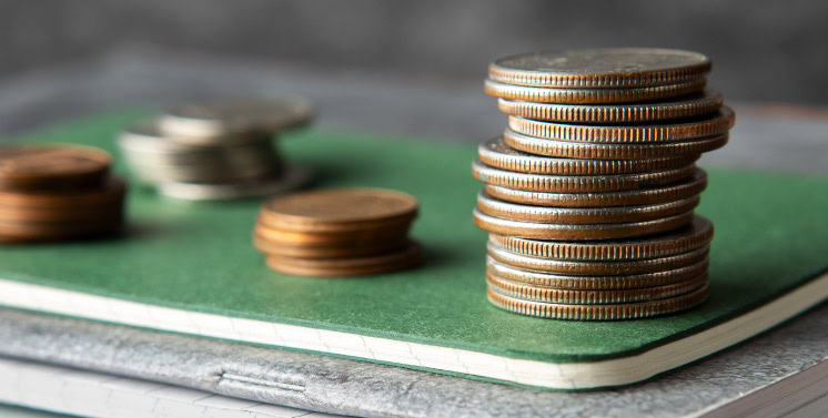 Moedas empilhadas ao lado de um livro sobre finanças, simbolizando gestão financeira e impostos, promovendo soluções financeiras confiáveis e eficientes da Dootax.