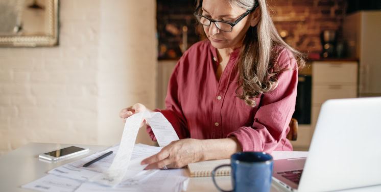 Declaração de Impostos em Casa, Mulher Revisando Documentos Fiscais com Lap Top e Smartphone, Organização Financeira, Serviços de Consultoria Fiscal com Dootax, Soluções Tributárias Digitais.